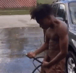 A Shirtless Man Is Washing A Car With A Hose In A Driveway . GIF