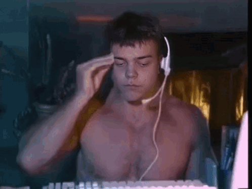 A Shirtless Man Is Wearing Headphones And A Headset While Sitting In Front Of A Computer Keyboard . GIF