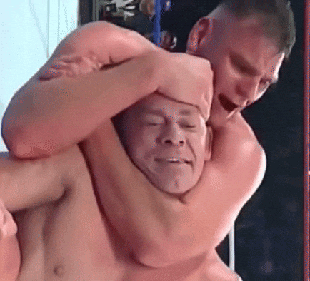 A Shirtless Man Is Wrestling Another Shirtless Man In A Ring With His Eyes Closed GIF