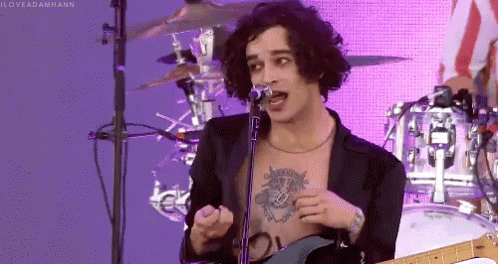 A Shirtless Man Singing Into A Microphone With A Tattoo On His Chest GIF