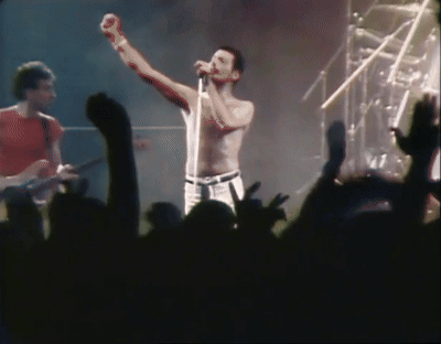 A Shirtless Man Singing Into A Microphone With His Fist In The Air GIF