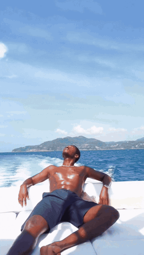 A Shirtless Man Sits On A Boat Looking Up At The Sky GIF