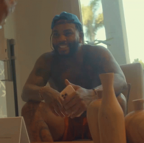 A Shirtless Man Sitting On A Couch Holding A Phone GIF