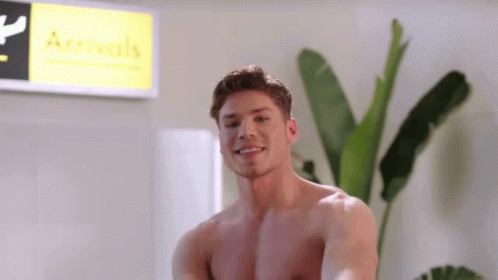 A Shirtless Man Smiles In Front Of A Sign That Says Arrivals GIF