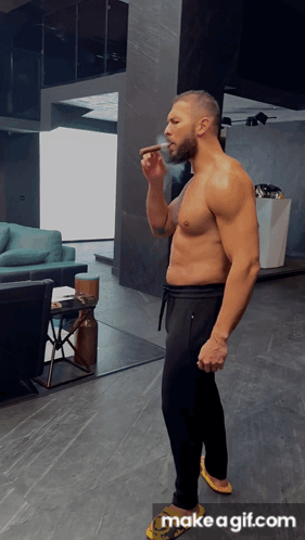 A Shirtless Man Smoking A Cigar In A Living Room With Make A Gif.com On The Bottom GIF