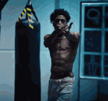 A Shirtless Man Standing Next To A Punching Bag GIF