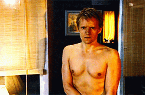 A Shirtless Man Stands In A Bathroom With A Picture On The Wall Behind Him GIF