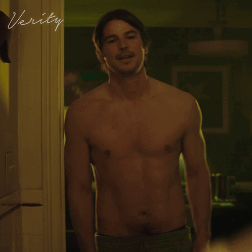A Shirtless Man Stands In A Doorway With The Word Verity Written On The Wall GIF