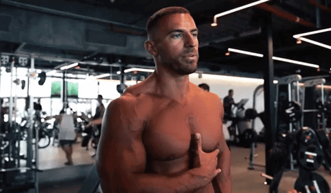 A Shirtless Man Stands In A Gym With His Hands On His Chest GIF