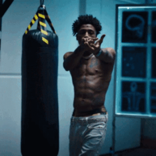 A Shirtless Man Stands In Front Of A Boxing Bag GIF