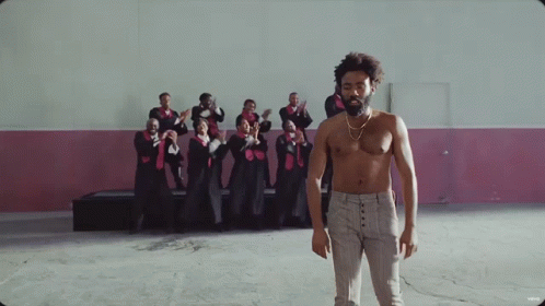 A Shirtless Man Stands In Front Of A Choir GIF