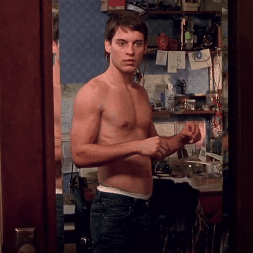 A Shirtless Man Stands In Front Of A Mirror In A Room GIF