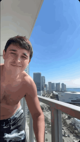 A Shirtless Man Stands On A Balcony With A City In The Background GIF