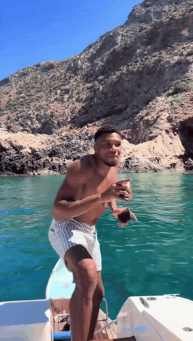 A Shirtless Man Stands On A Boat In The Ocean GIF