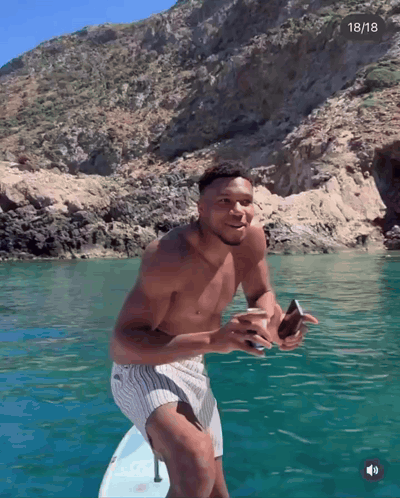 A Shirtless Man Stands On A Surfboard In The Water With The Date 18/18 In The Corner GIF