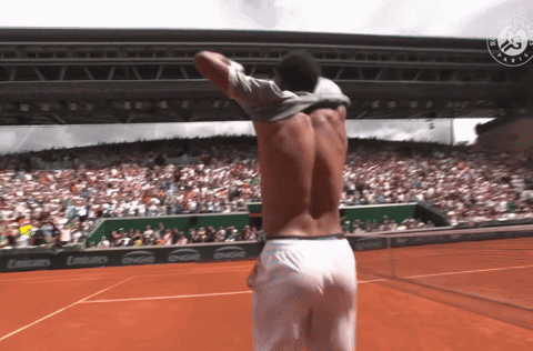 a shirtless man stands on a tennis court in front of a crowd and a coca cola banner