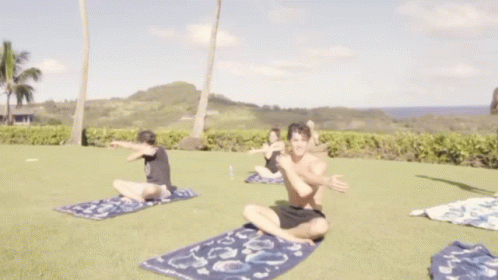 A Shirtless Man Stretches His Arms While A Woman Sits On The Grass GIF