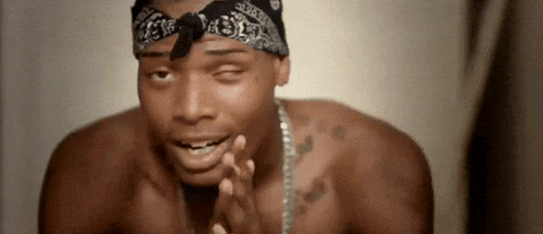 A Shirtless Man Wearing A Bandana And A Chain Is Praying . GIF