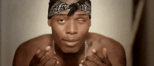 A Shirtless Man Wearing A Bandana And A Necklace Is Making A Face . GIF