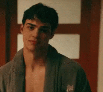 A Shirtless Man Wearing A Bathrobe Is Standing In Front Of A Door . GIF