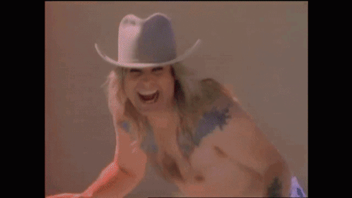 A Shirtless Man Wearing A Cowboy Hat Is Laughing . GIF