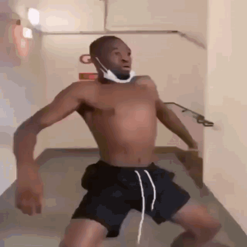 A Shirtless Man Wearing A Mask And Shorts Is Standing In A Hallway . GIF