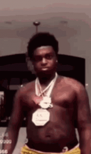 A Shirtless Man Wearing A Medal Around His Neck Is Standing In A Room . GIF
