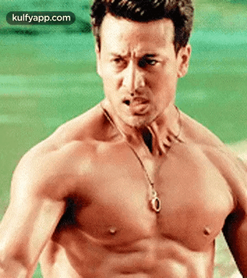 A Shirtless Man Wearing A Necklace And A Pendant On His Chest . GIF