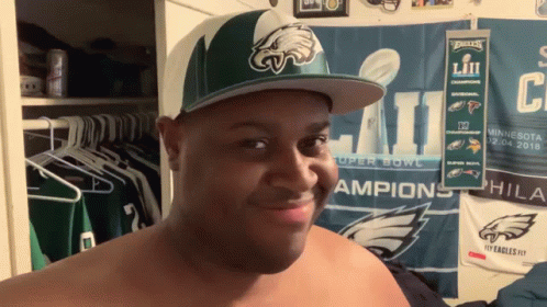 A Shirtless Man Wearing A Philadelphia Eagles Hat Looks At The Camera GIF