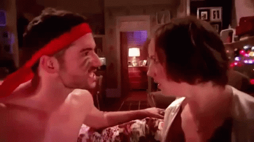 A Shirtless Man Wearing A Red Headband Is Fighting A Woman In A Bedroom . GIF