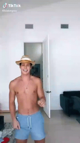 A Shirtless Man Wearing A Straw Hat And Blue Shorts Is Dancing In A Room . GIF