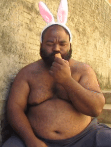 A Shirtless Man Wearing Bunny Ears Is Eating An Ice Cream GIF