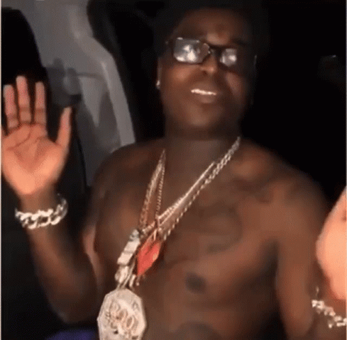 A Shirtless Man Wearing Glasses And A Necklace Is Waving His Hands . GIF