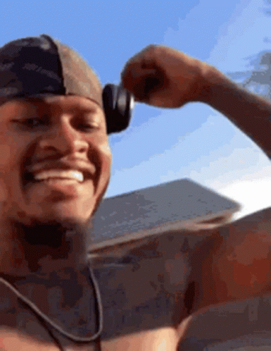 A Shirtless Man Wearing Headphones Is Smiling And Flexing His Arm . GIF