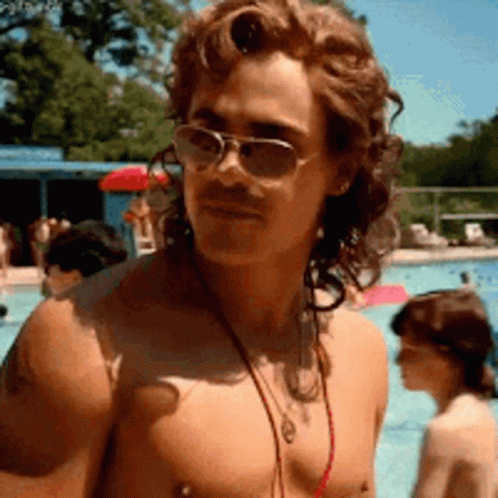 A Shirtless Man Wearing Sunglasses And A Necklace Is Standing In Front Of A Swimming Pool . GIF