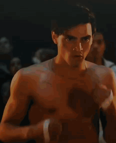 A Shirtless Man With A Bandage On His Wrist Is Standing In A Dark Room With Other Men . GIF