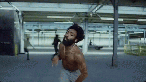 A Shirtless Man With A Beard Is Dancing In A Parking Lot . GIF