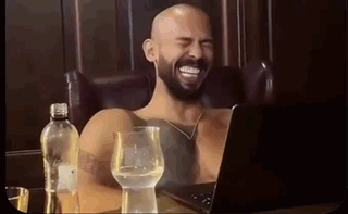 A Shirtless Man With A Beard Is Laughing While Sitting In Front Of A Laptop . GIF