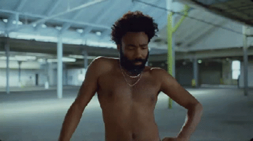 A Shirtless Man With A Beard Is Standing In An Empty Warehouse GIF