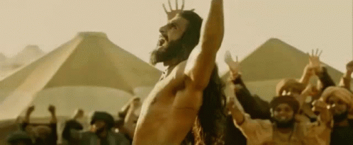 A Shirtless Man With A Beard Is Standing In Front Of A Crowd Of People . GIF