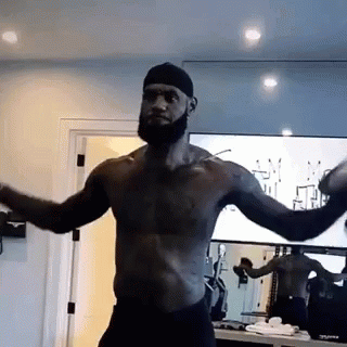 A Shirtless Man With A Beard Is Standing In Front Of A Mirror In A Gym . GIF