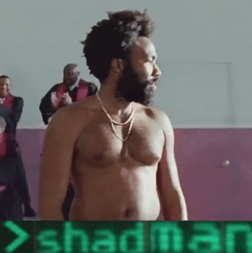 A Shirtless Man With A Beard Is Standing In Front Of A Sign That Says Shadman .. GIF