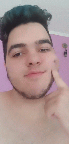 A Shirtless Man With A Beard Points To His Face With His Finger GIF
