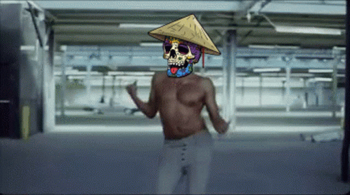 A Shirtless Man With A Colorful Skull On His Face Wearing A Conical Hat GIF