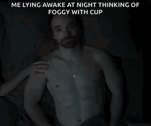 A Shirtless Man With A Cross Necklace Is Laying In The Dark GIF