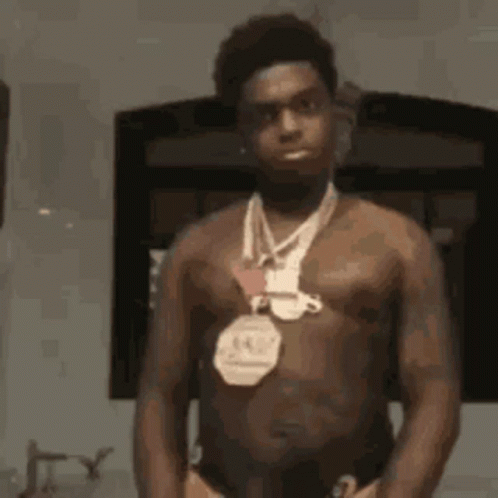 A Shirtless Man With A Medal Around His Neck Is Standing In Front Of A Mirror . GIF