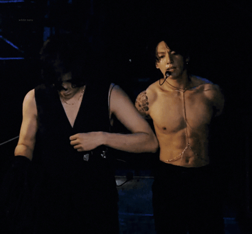 a shirtless man with a microphone around his neck looks at the camera