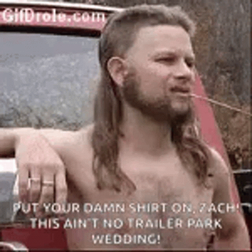 A Shirtless Man With A Mullet And A Beard Is Smoking A Cigarette In Front Of A Car . GIF