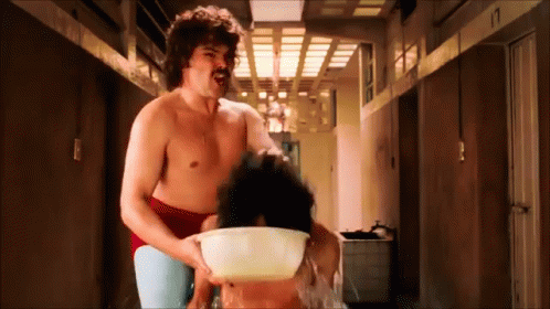 A Shirtless Man With A Mustache Is Holding A Bowl Of Water Over A Woman 'S Head GIF