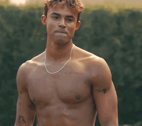 A Shirtless Man With A Necklace Around His Neck Has A Tattoo On His Chest That Says ' X ' On It GIF